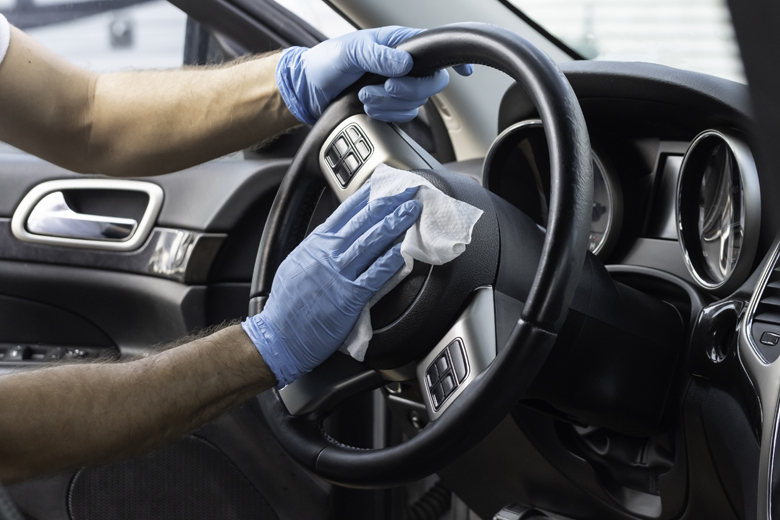 Un mécanicien lave un volant avec des gants et des lingettes désinfectantes.